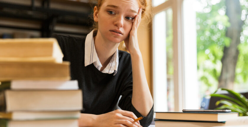 A student looks stressed as she looks at a stack of books_NCLEX Classes